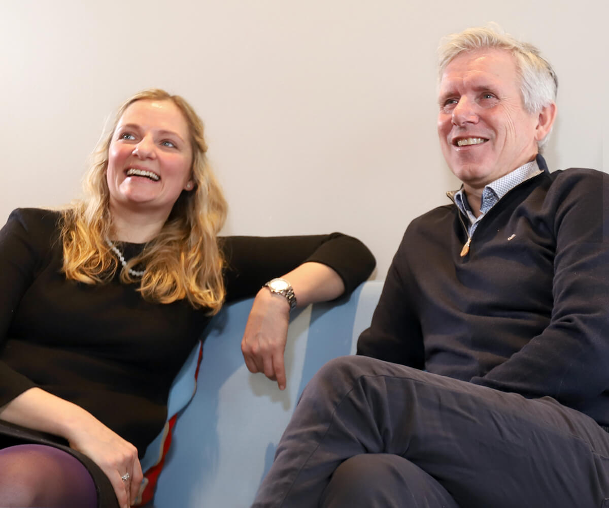 Smilende mand og kvinde sidder afslappet i en sofa på kontoret